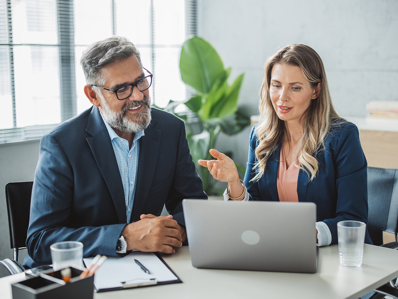 Two colleagues discussing sitting at an office table looking at a laptop