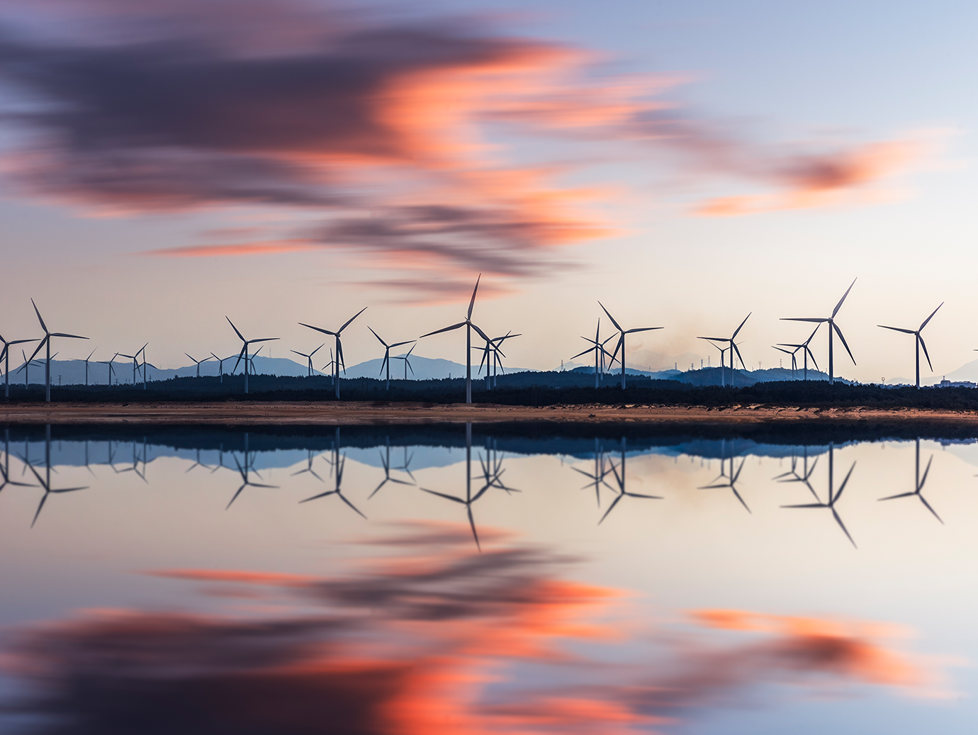 A wind farm across a lake at dusk