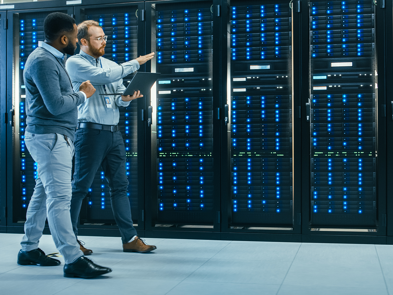 Two men with a laptop walking in a data server room