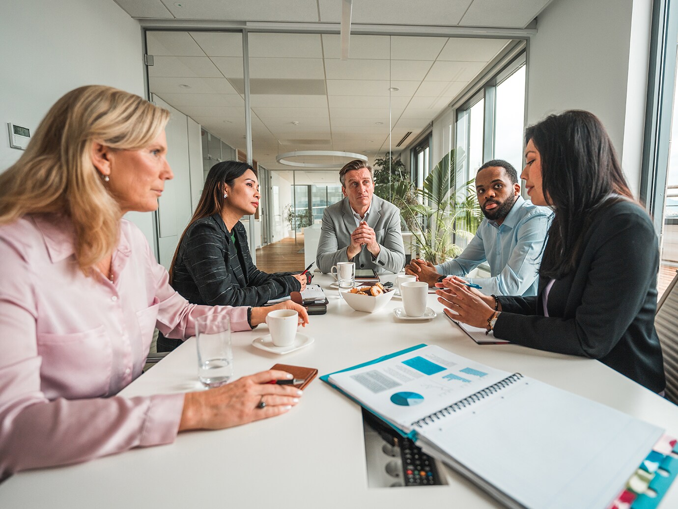 Five people in discussion at a table with documents spread out