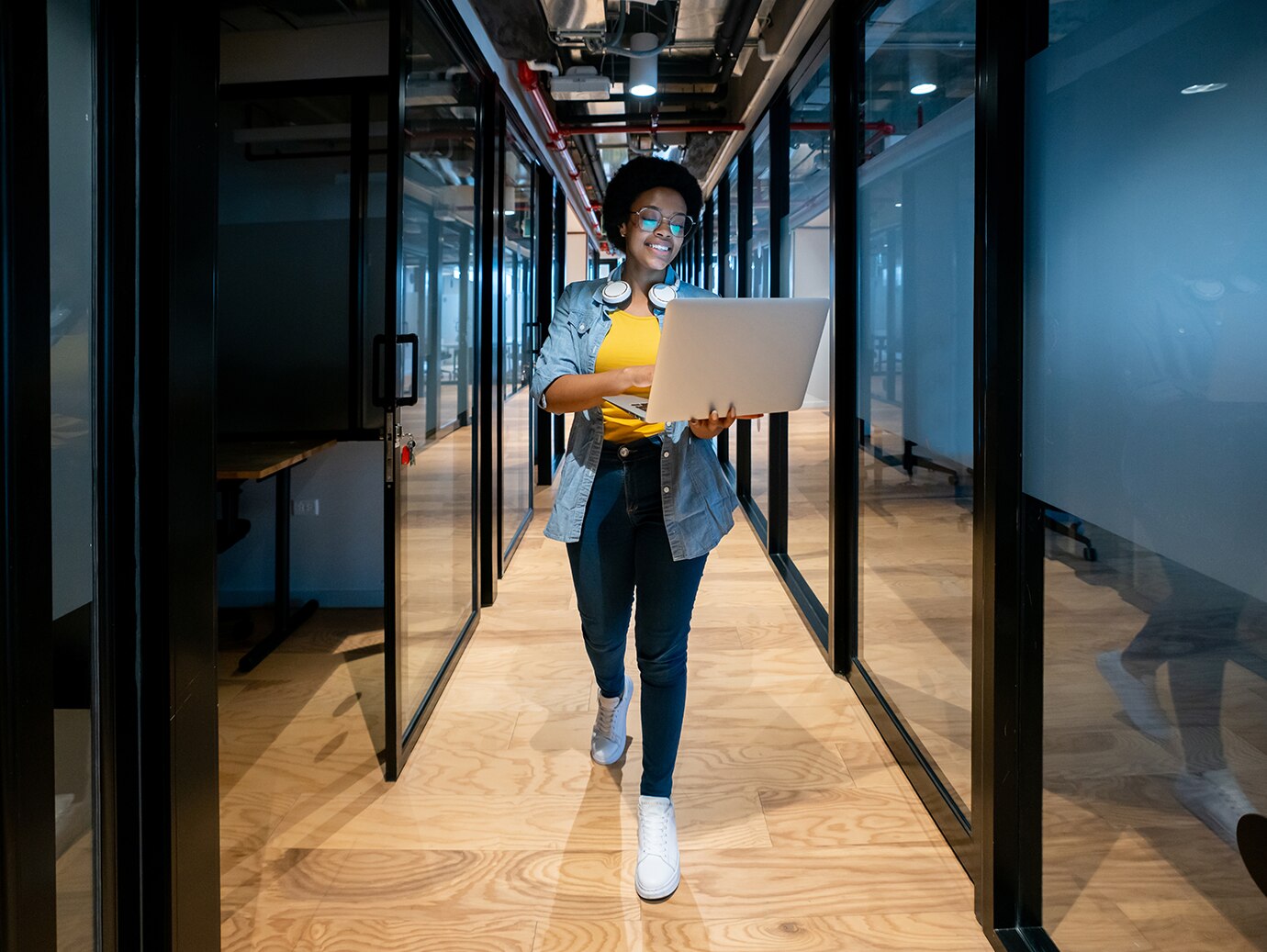 A woman walking in a lobby between conference rooms holding a laptop