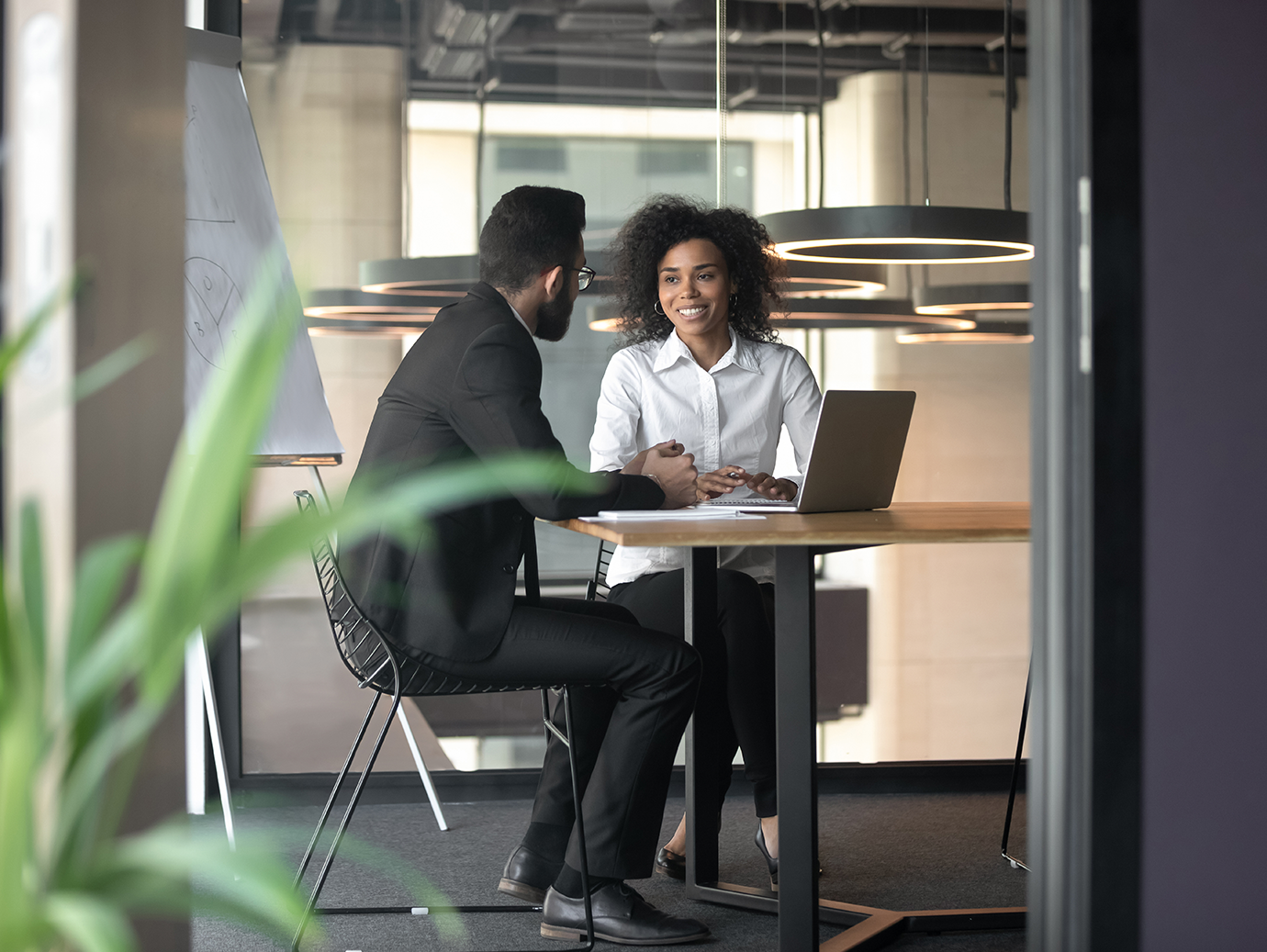 Two people in formal attire having a discussion sitting at a conference table