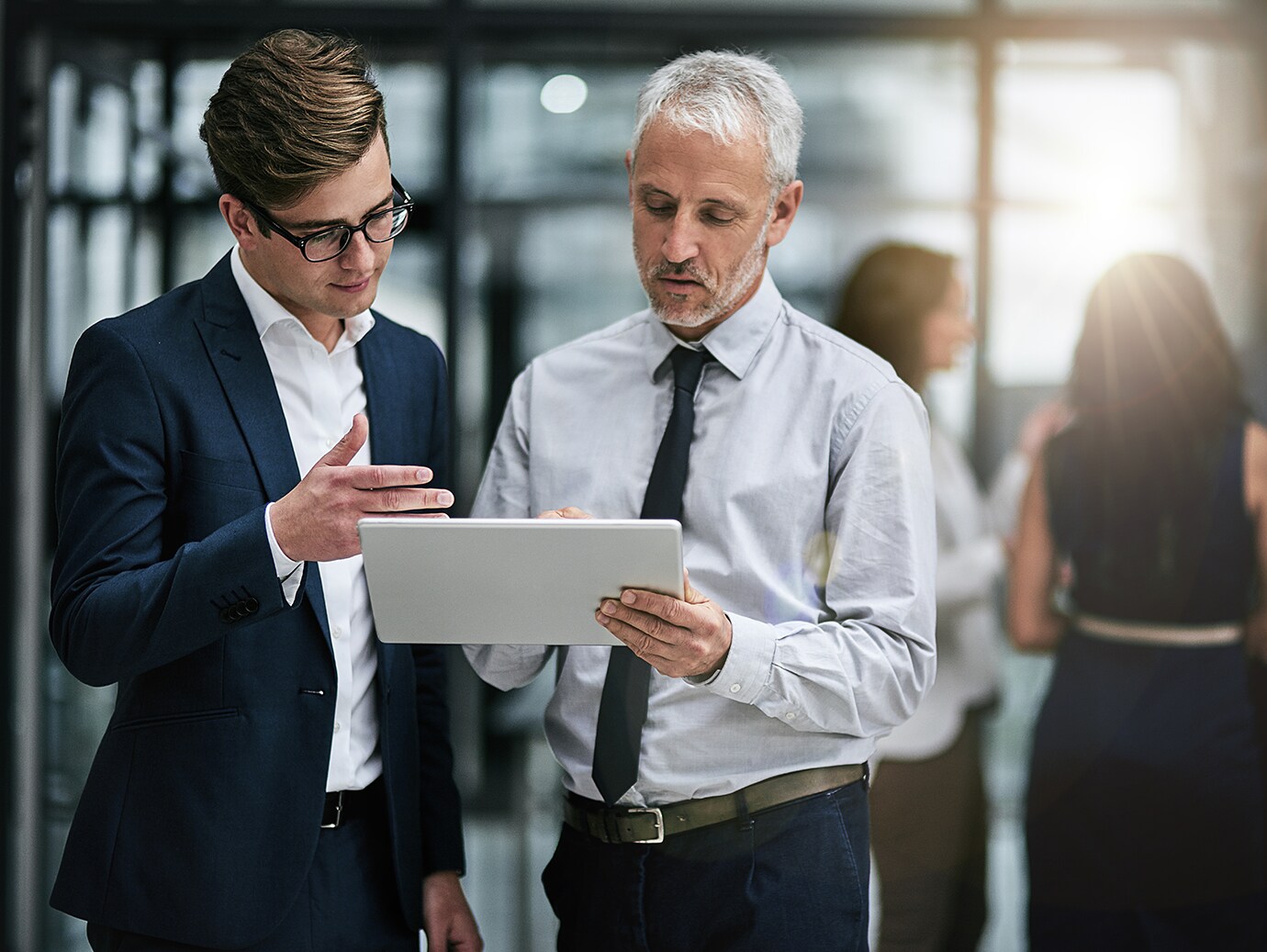 Two colleagues looking at a tablet and conversing in an office lobby