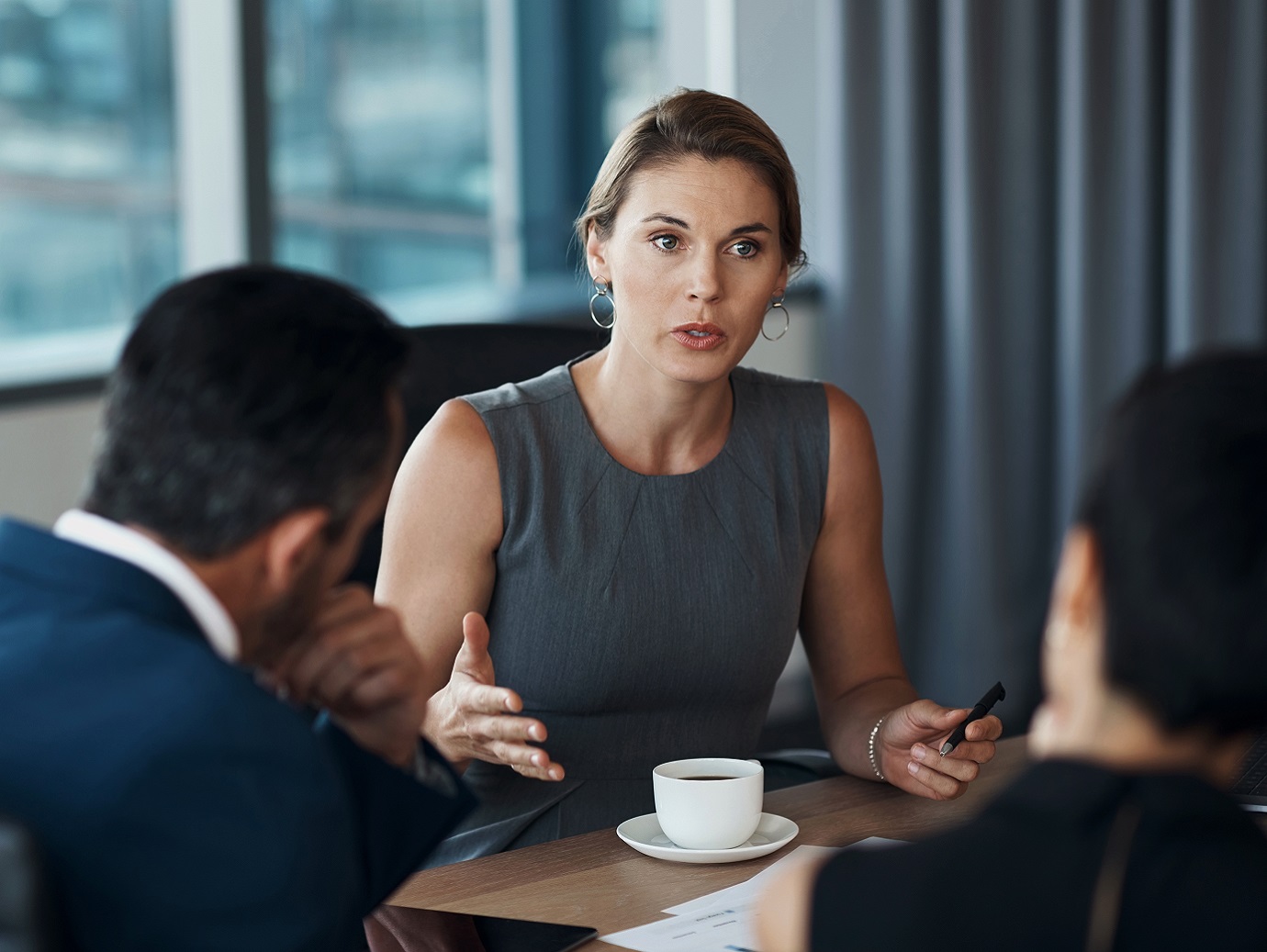 A lady involved in a discussion with two men in a conference room