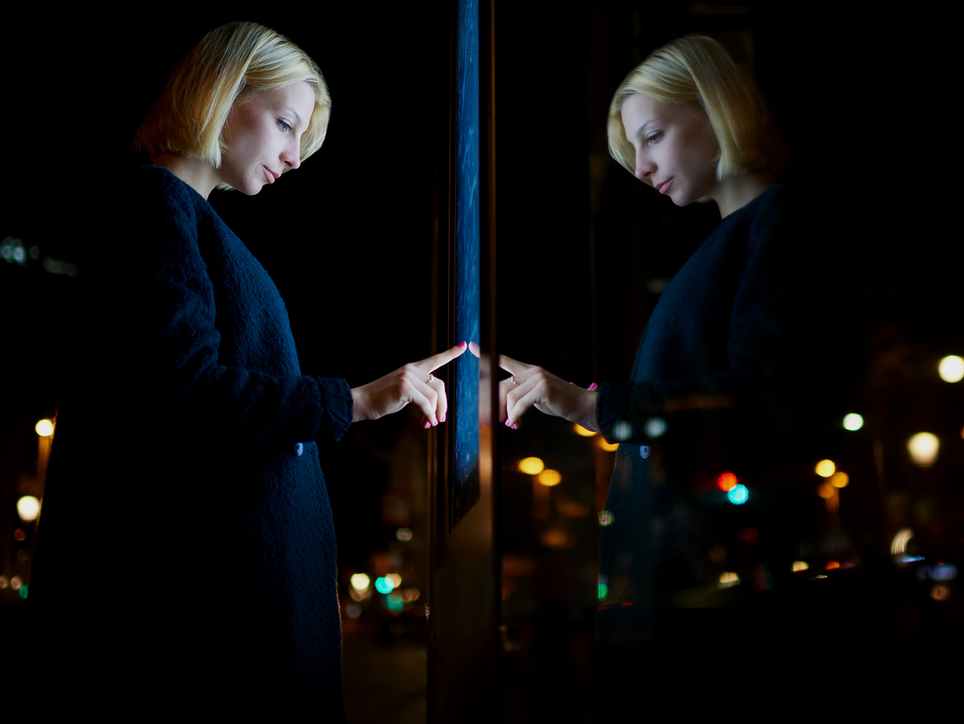 Woman's face illuminated by light from a screen in front of a full length glass window