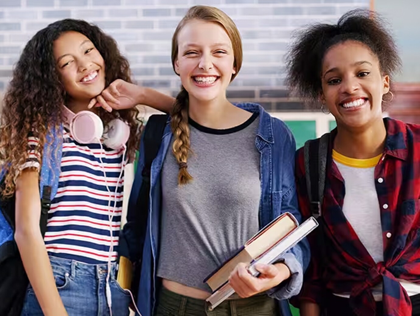 Three high-school girls wearing backpacks smiling at the camera