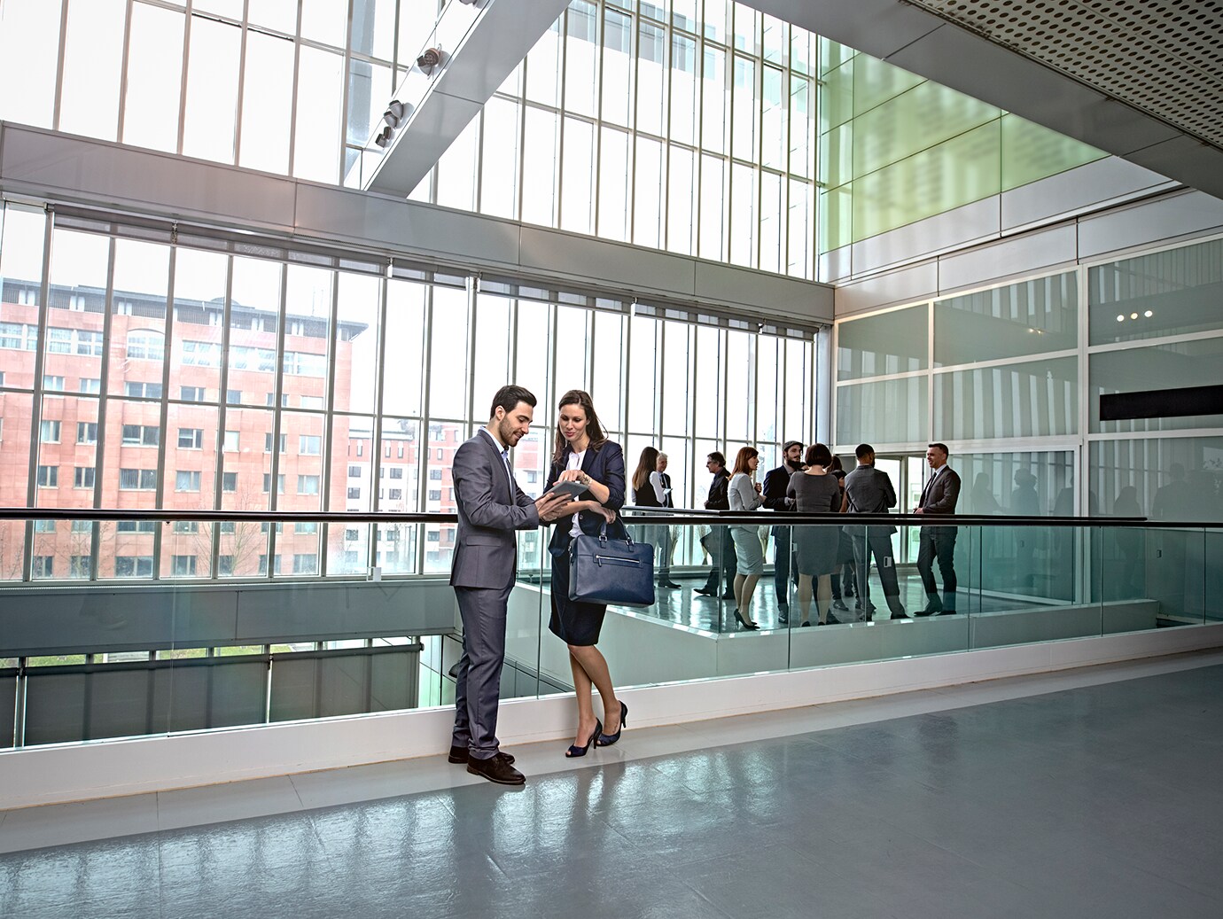 Two colleagues discussing leaning over a railing in office lounge