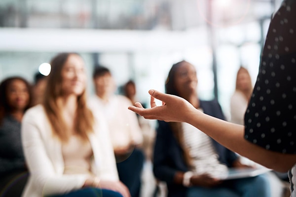 A blurred classroom scenario where a professor is giving lecture to his students sitting infront of her.