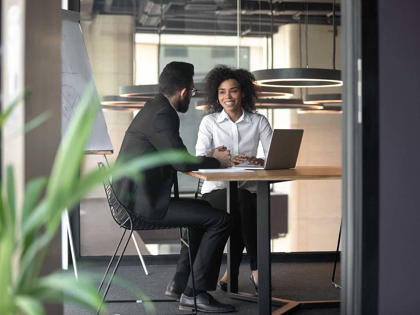 Two people in formal attire having a discussion sitting at a conference table