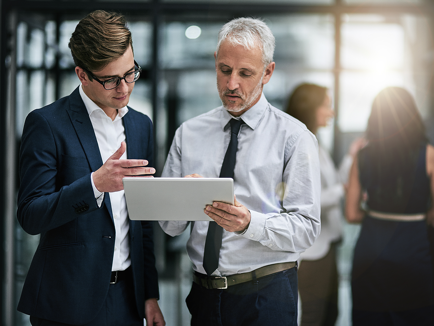 Two colleagues looking at a tablet and conversing in an office lobby
