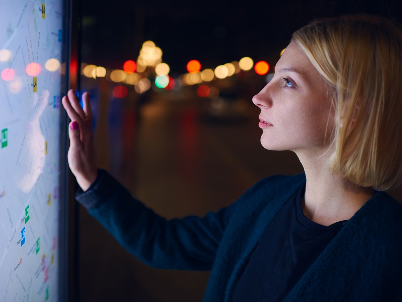 A lady looking closely looking at a big touch screen infront of her which displays a map.