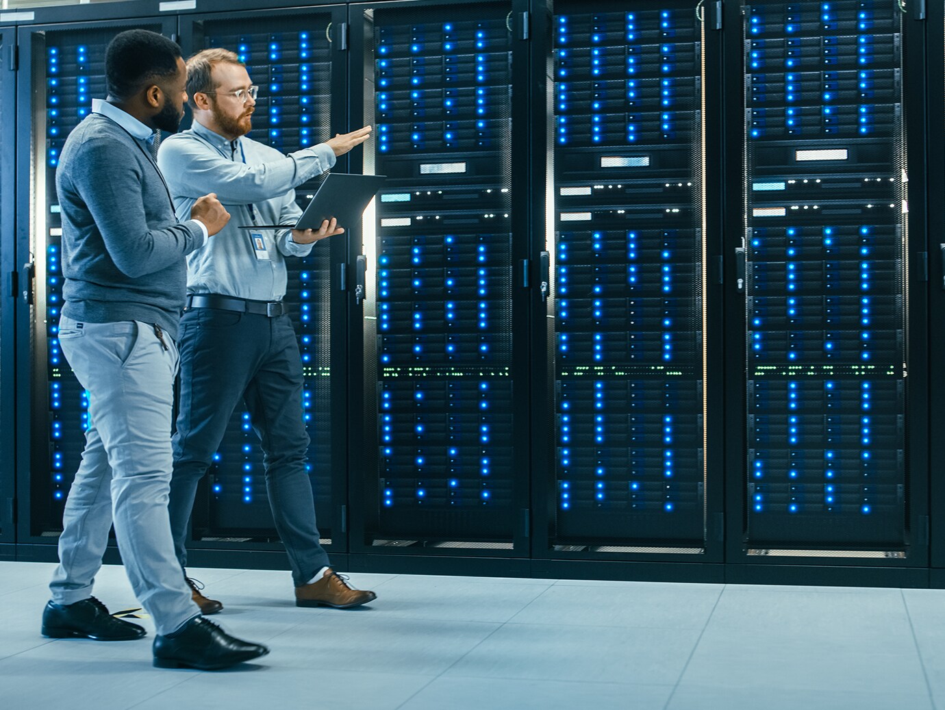 Two men with a laptop walking in a data server room